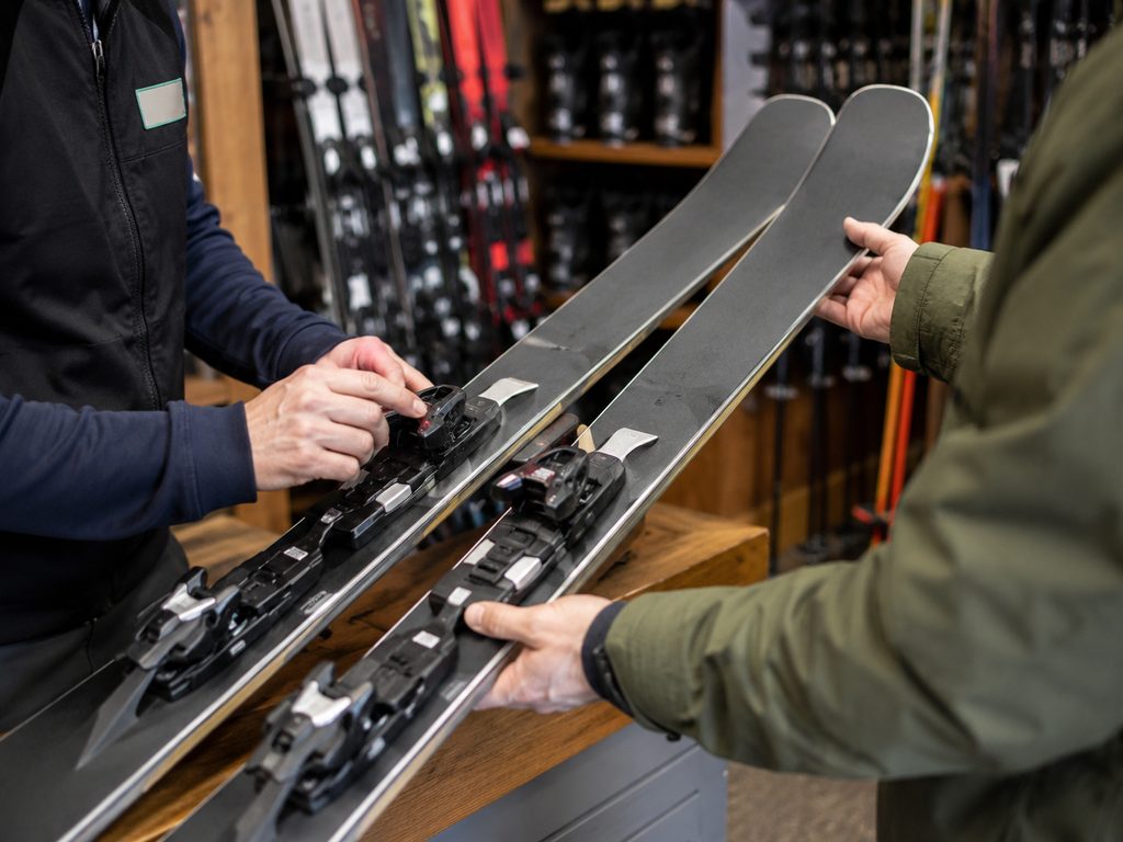 Mitarbeiter im Skiverleih stellt die Bindung eines Leihski für einen Kunden ein